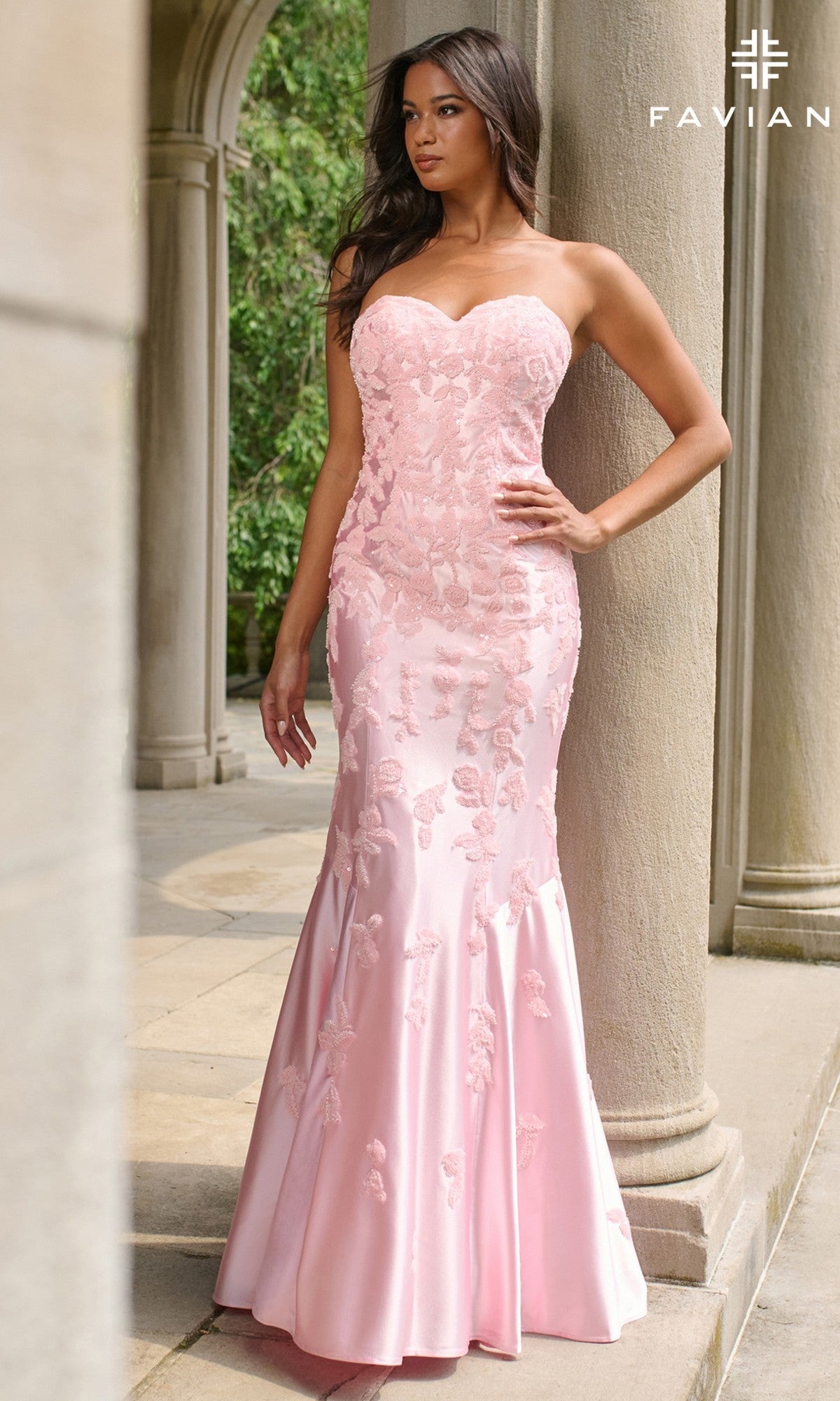 A woman stands outdoors wearing the Faviana 11271 long prom dress, a strapless, floor-length mermaid gown in light pink with delicate floral embroidery.